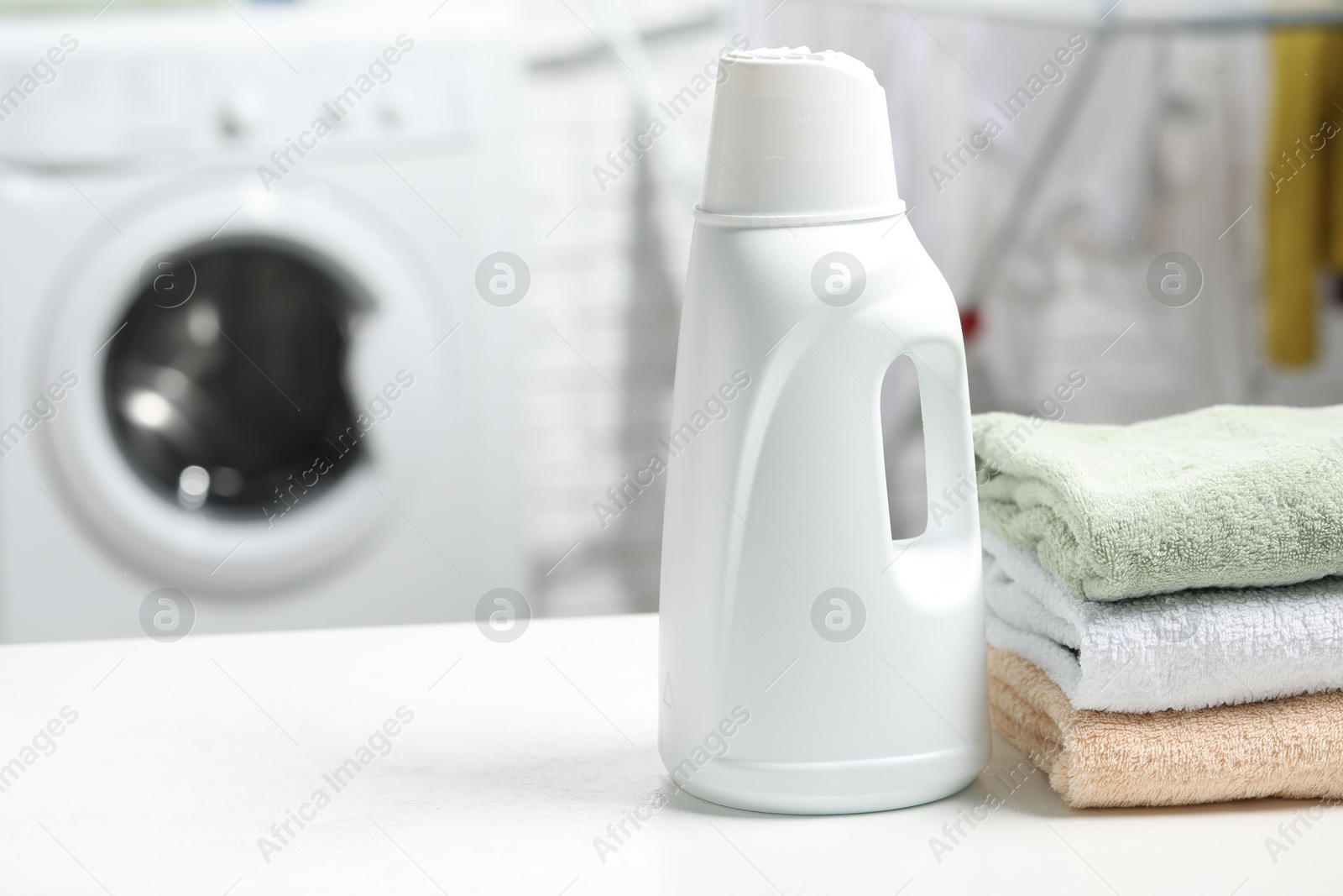 Photo of Laundry detergent and stacked clean towels on white table, space for text