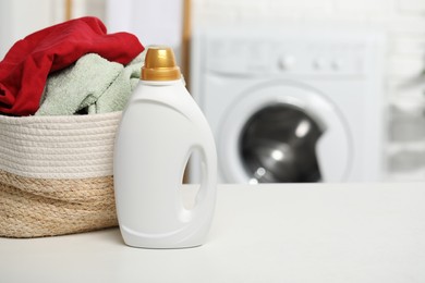 Photo of Detergent and basket with towels on white table in bathroom, space for text