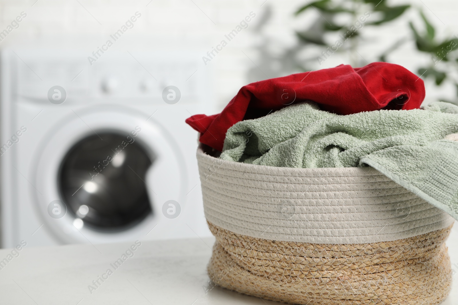 Photo of Basket full of laundry on white table in bathroom, space for text