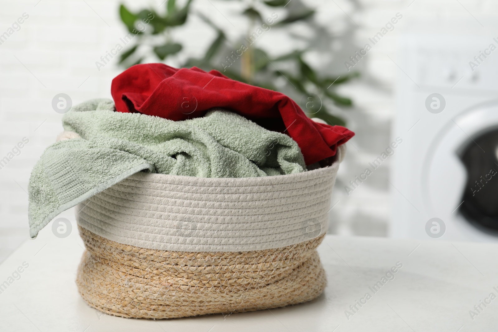 Photo of Basket full of laundry on white table in bathroom. Space for text