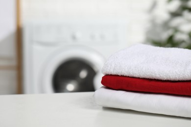 Photo of Stacked clean laundry on white table in bathroom, space for text