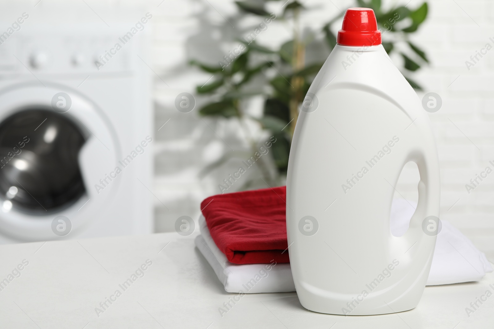 Photo of Detergent and basket with towels on white table in bathroom, space for text