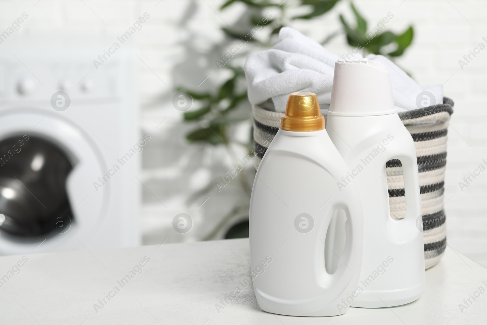 Photo of Detergents and basket with towels on white table in bathroom, space for text