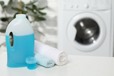 Photo of Laundry detergent, cap and rolled towels on white table in bathroom, space for text