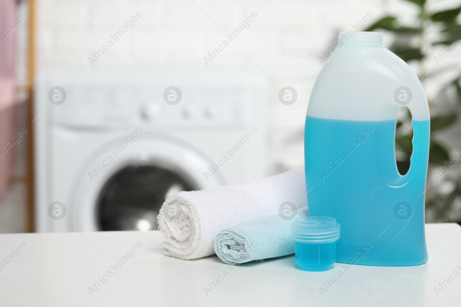 Photo of Laundry detergent, cap and rolled towels on white table in bathroom, space for text