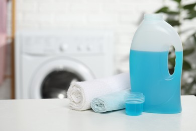 Photo of Laundry detergent, cap and rolled towels on white table in bathroom, space for text