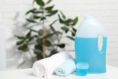 Photo of Laundry detergent, cap and rolled towels on white table in bathroom