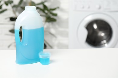 Photo of Laundry detergent and cap on white table in bathroom, space for text