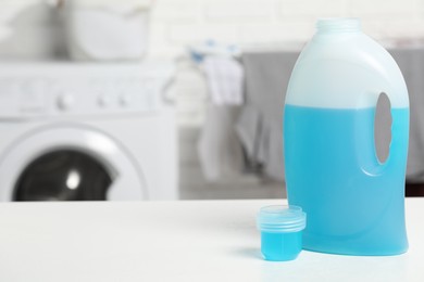 Photo of Laundry detergent and cap on white table in bathroom, space for text