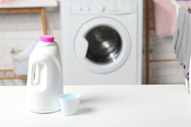 Photo of Laundry detergent and cap on white table in bathroom, space for text