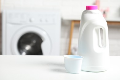 Photo of Laundry detergent and cap on white table in bathroom, space for text