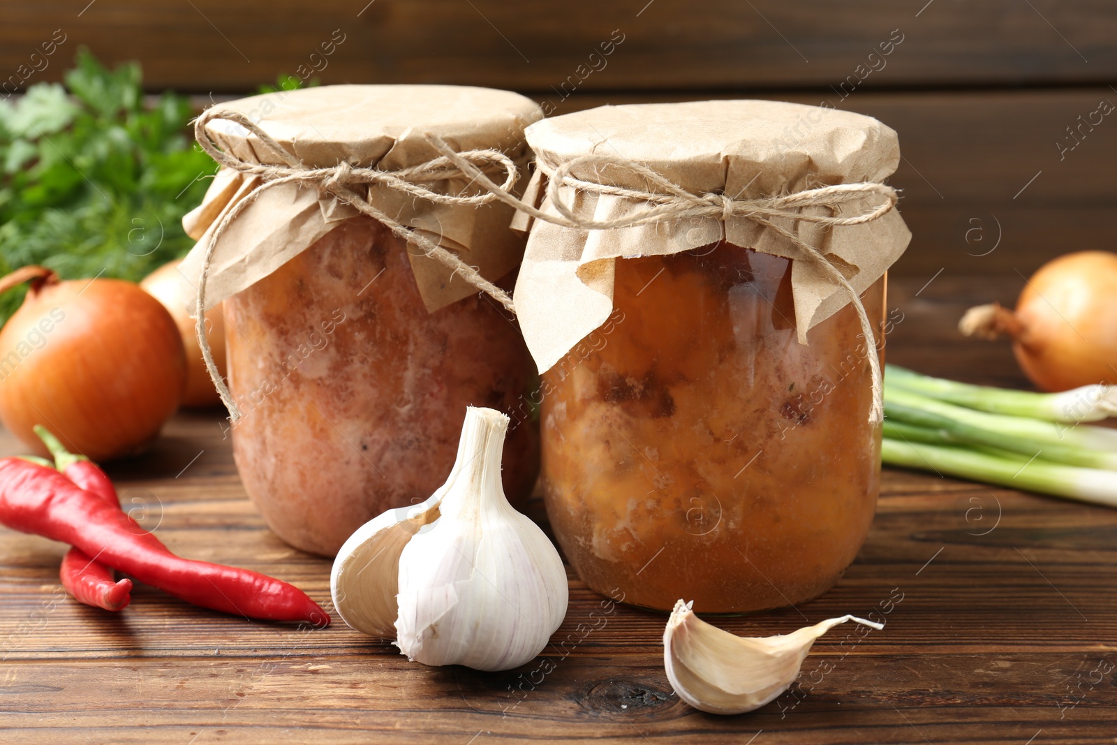 Photo of Canned meat in glass jars and fresh products on wooden table, closeup