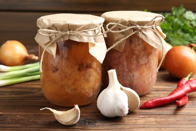 Photo of Canned meat in glass jars and fresh products on wooden table, closeup