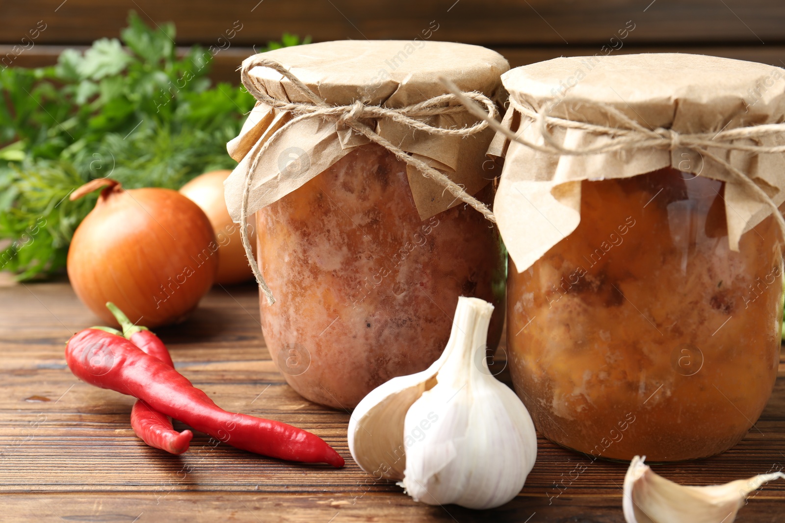 Photo of Canned meat in glass jars and fresh products on wooden table, closeup