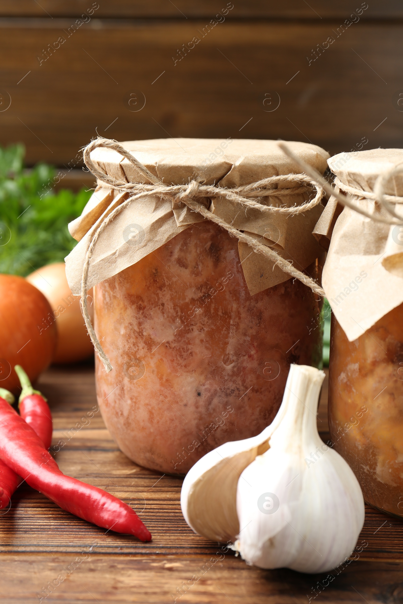 Photo of Canned meat in glass jars and fresh products on wooden table, closeup