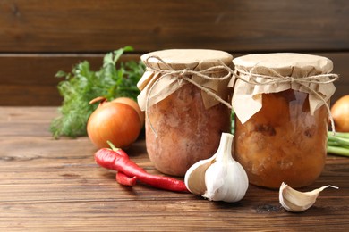 Photo of Canned meat in glass jars and fresh products on wooden table, space for text