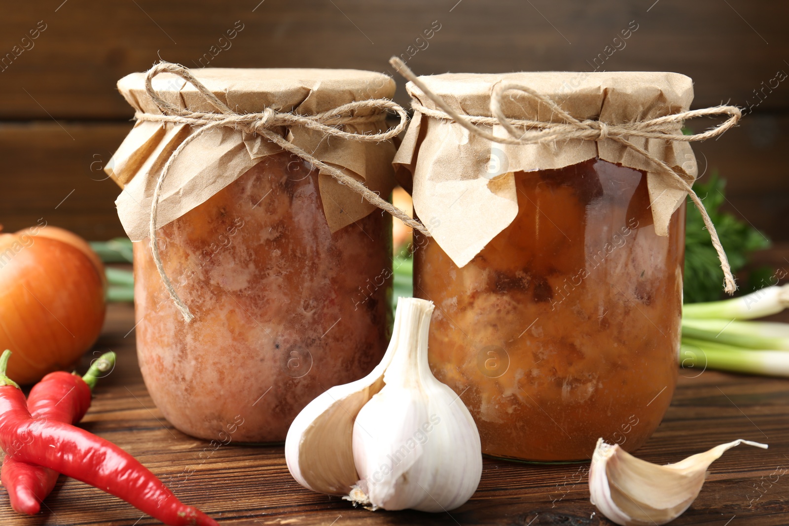 Photo of Canned meat in glass jars and fresh products on wooden table, closeup