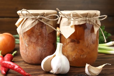 Canned meat in glass jars and fresh products on wooden table, closeup