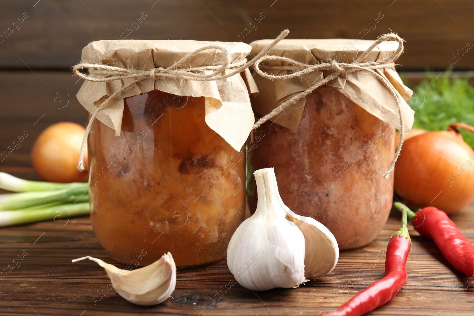 Photo of Canned meat in glass jars and fresh products on wooden table, closeup