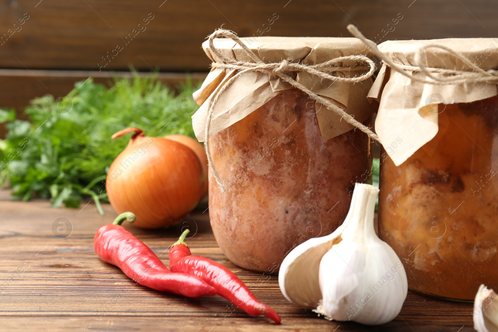 Photo of Canned meat in glass jars and fresh products on wooden table, closeup