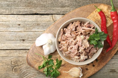 Photo of Canned meat in bowl and fresh products on wooden table, top view. Space for text