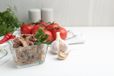 Photo of Canned meat with parsley in bowl and fresh vegetables on white wooden table, space for text