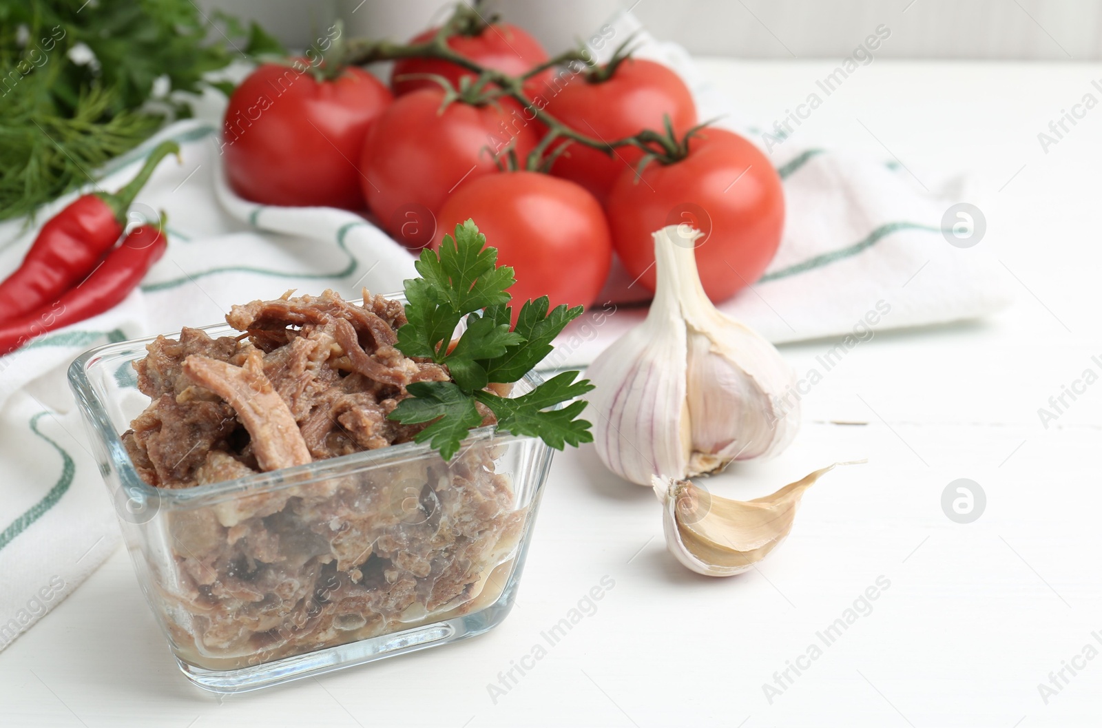 Photo of Canned meat with parsley in bowl and fresh vegetables on white wooden table, space for text