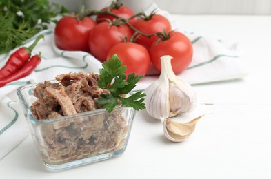 Photo of Canned meat with parsley in bowl and fresh vegetables on white wooden table, space for text