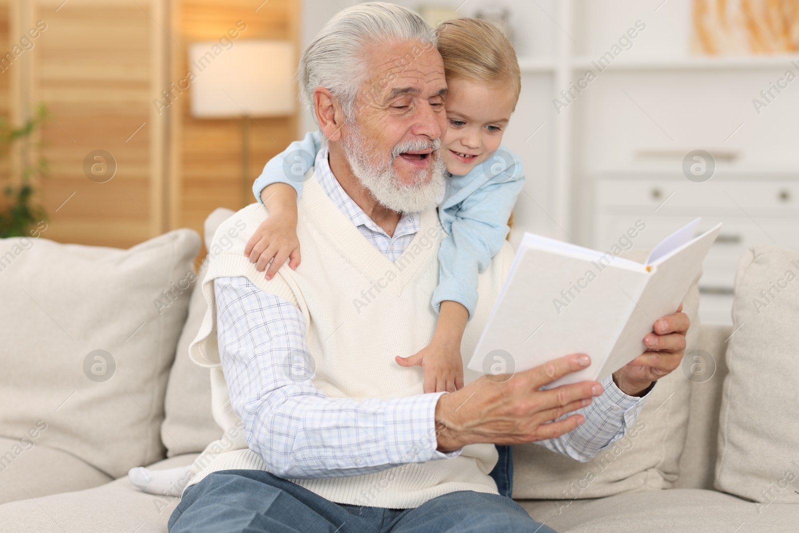 Photo of Grandpa and his granddaughter reading book together on sofa at home