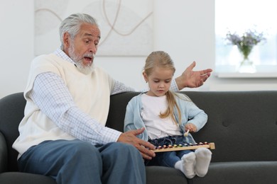 Photo of Grandpa and his granddaughter playing toy xylophone on sofa at home