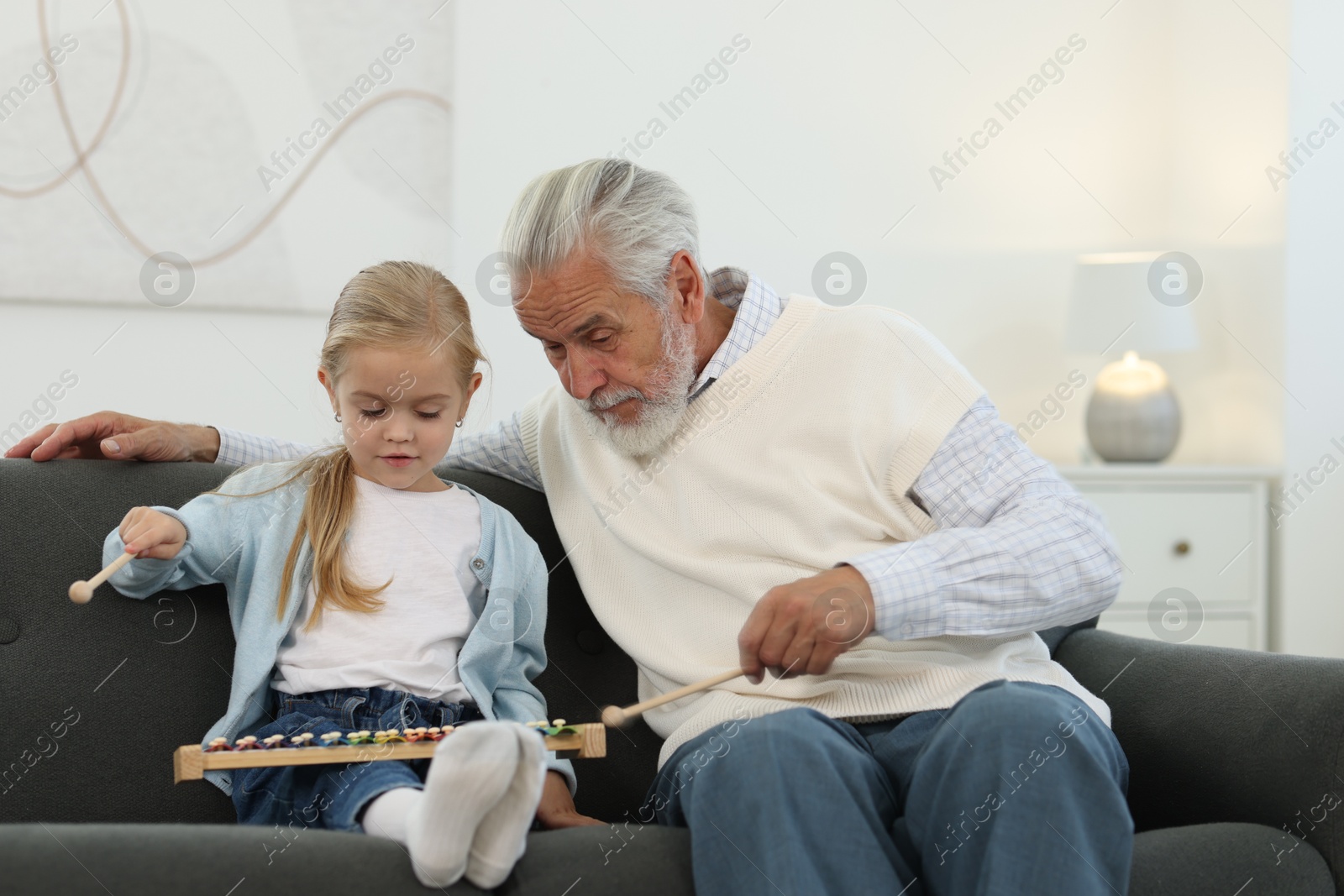 Photo of Grandpa and his granddaughter playing toy xylophone on sofa at home