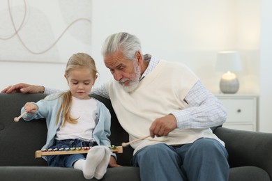 Photo of Grandpa and his granddaughter playing toy xylophone on sofa at home