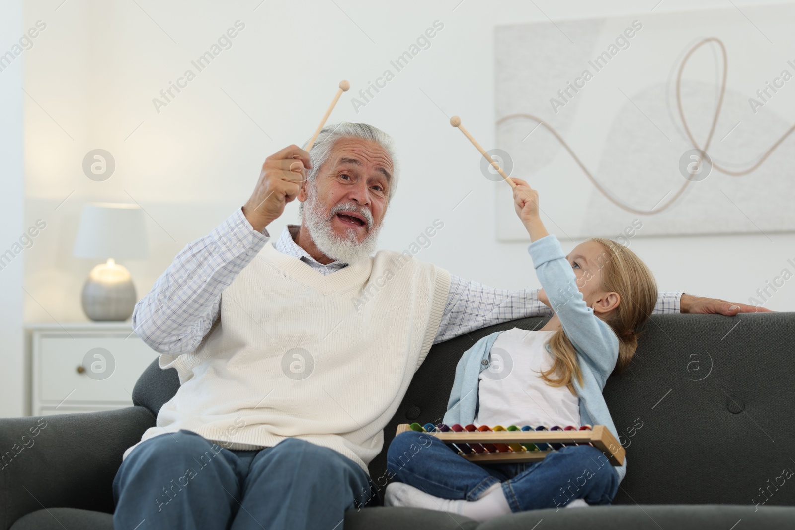 Photo of Grandpa and his granddaughter playing toy xylophone on sofa at home