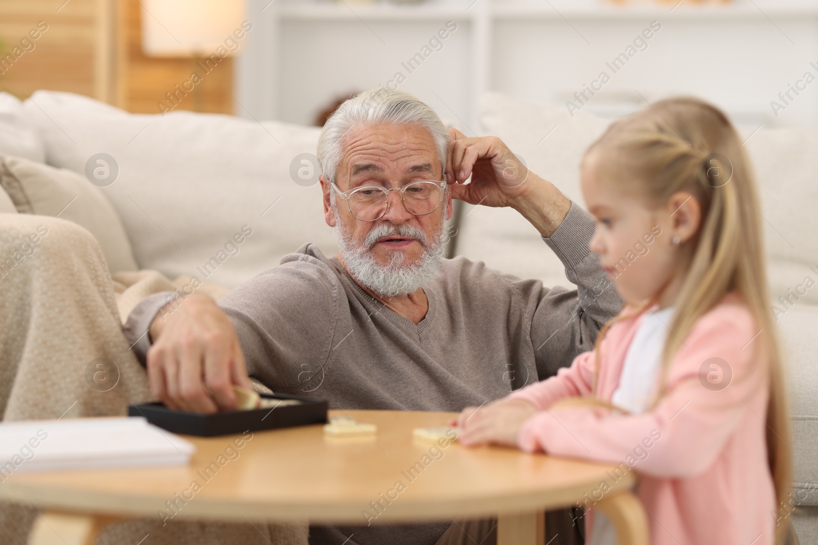 Photo of Grandpa and his granddaughter playing dominoes at table indoors