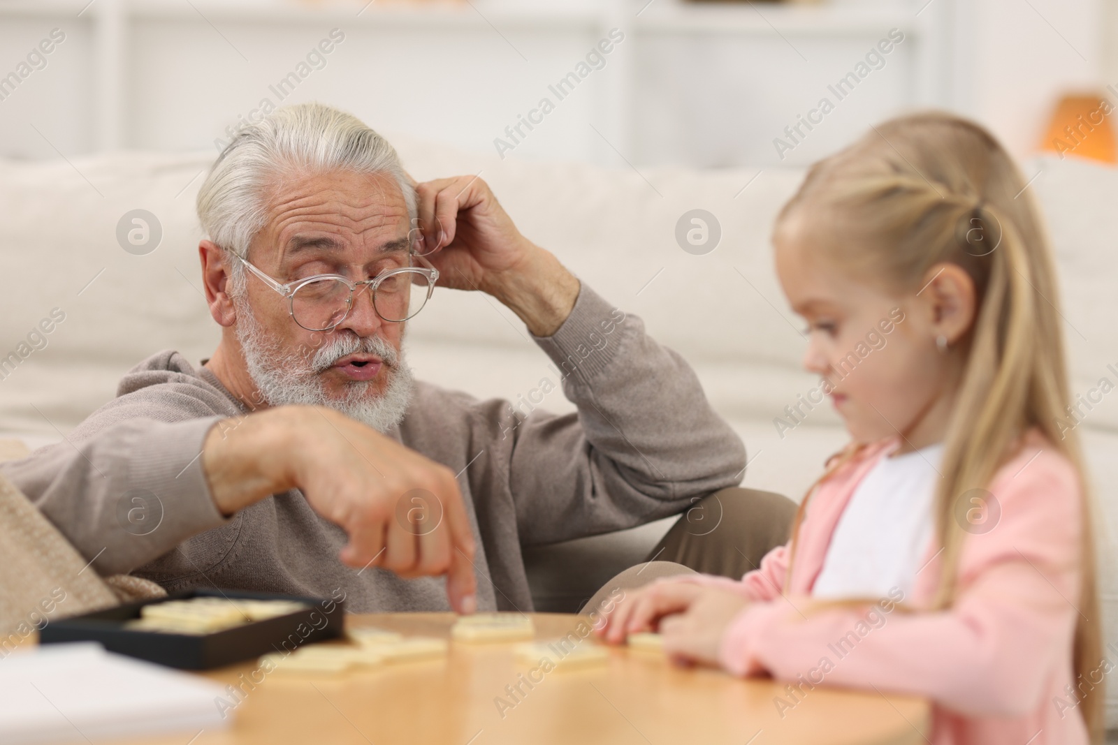 Photo of Grandpa and his granddaughter playing dominoes at table indoors