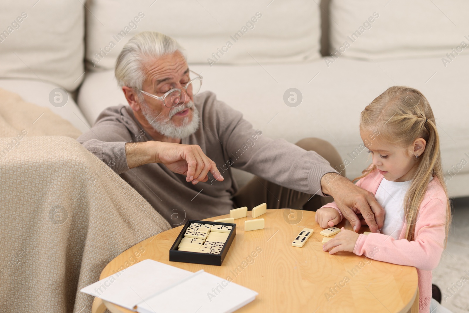 Photo of Grandpa and his granddaughter playing dominoes at table indoors