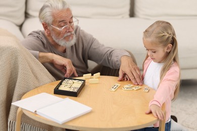 Grandpa and his granddaughter playing dominoes at table indoors