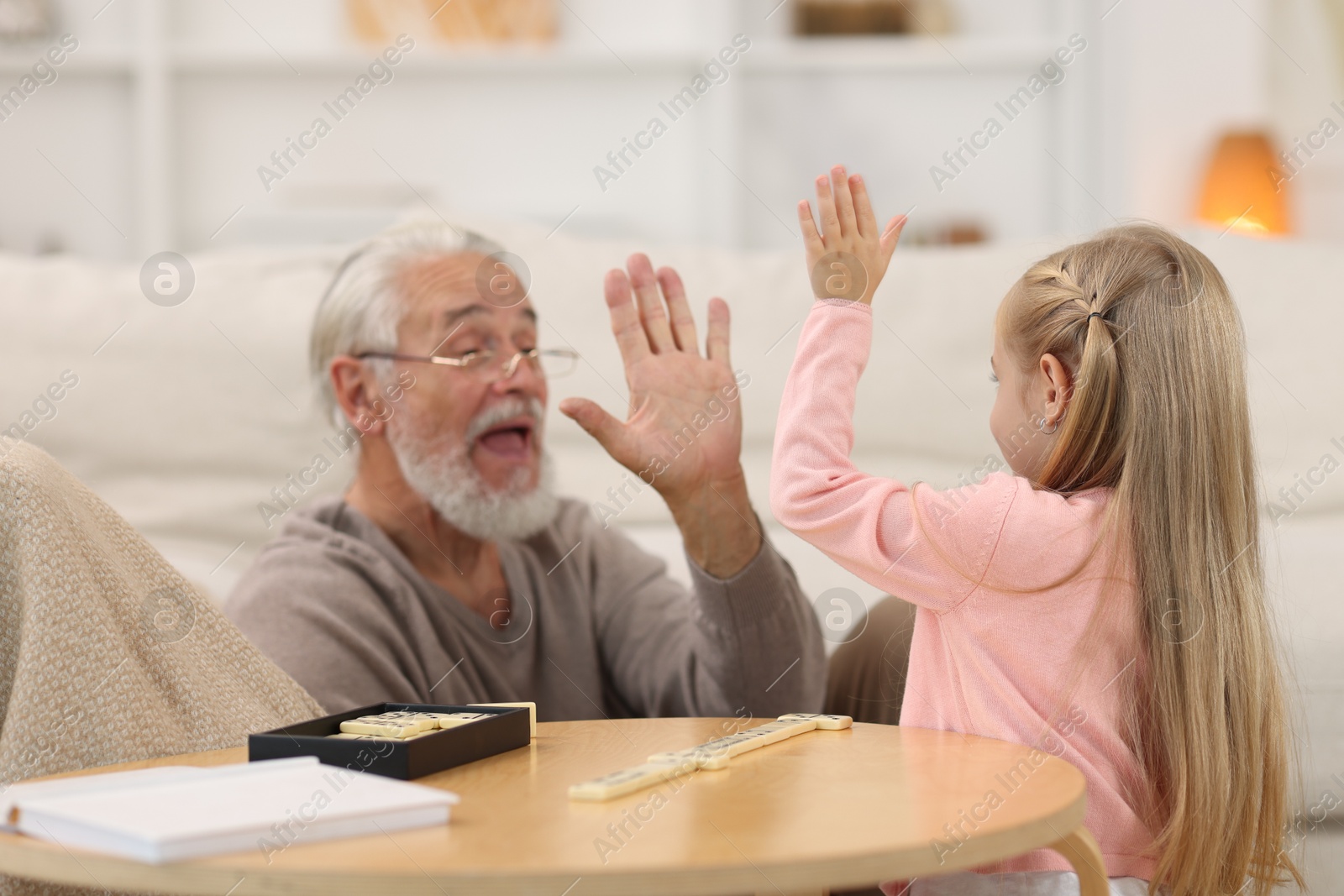 Photo of Grandpa and his granddaughter playing dominoes at table indoors