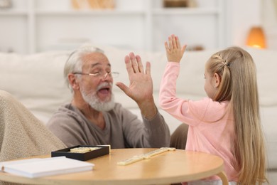 Grandpa and his granddaughter playing dominoes at table indoors