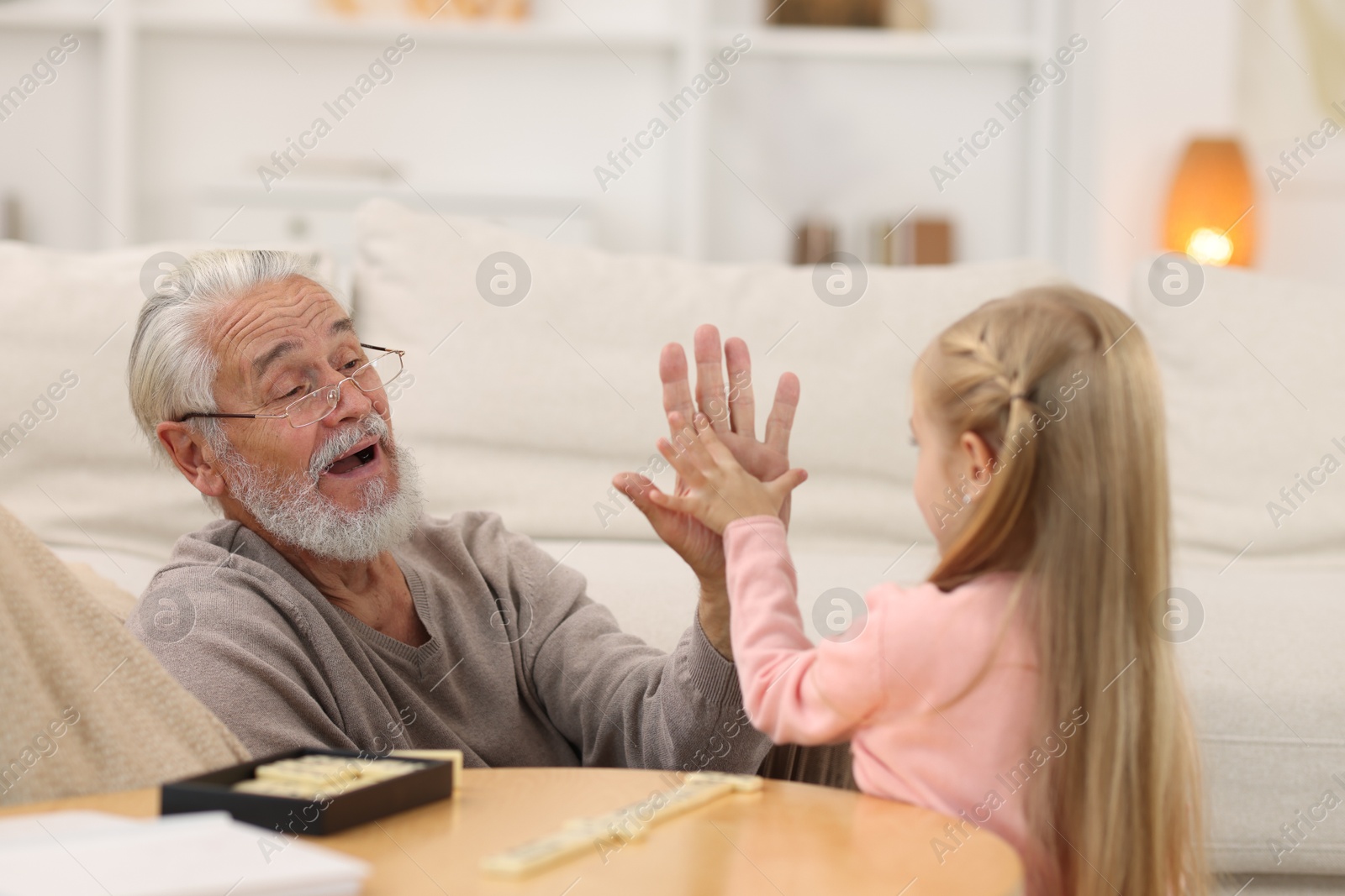 Photo of Grandpa and his granddaughter playing dominoes at table indoors