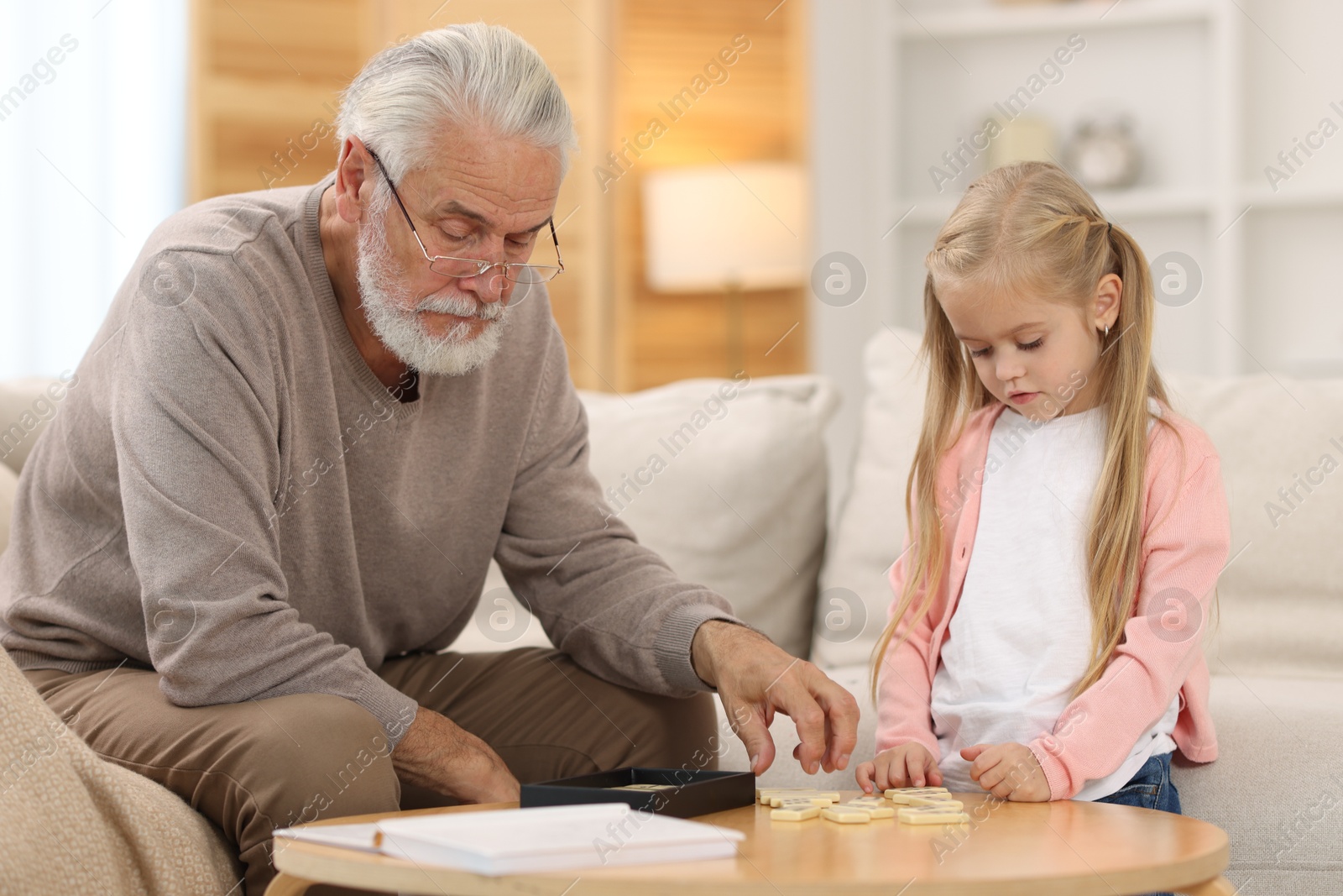 Photo of Grandpa and his granddaughter playing dominoes at table indoors