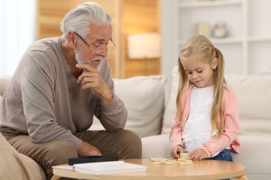 Photo of Grandpa and his granddaughter playing dominoes at table indoors