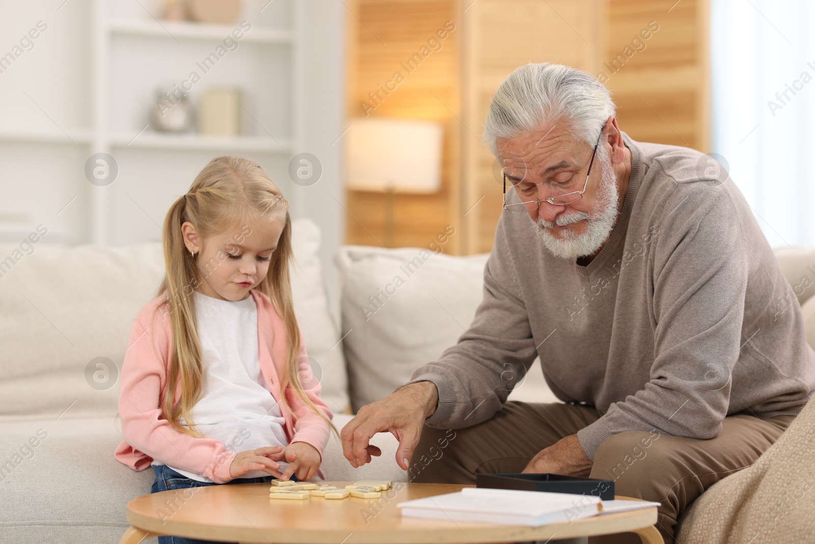 Photo of Grandpa and his granddaughter playing dominoes at table indoors