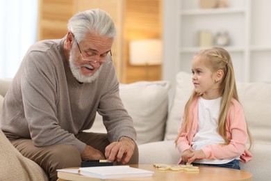 Grandpa and his granddaughter playing dominoes at table indoors