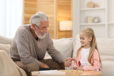 Grandpa and his granddaughter playing dominoes at table indoors