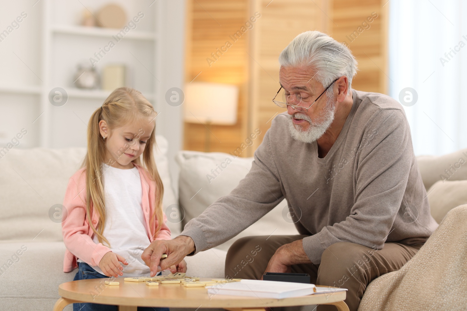 Photo of Grandpa and his granddaughter playing dominoes at table indoors