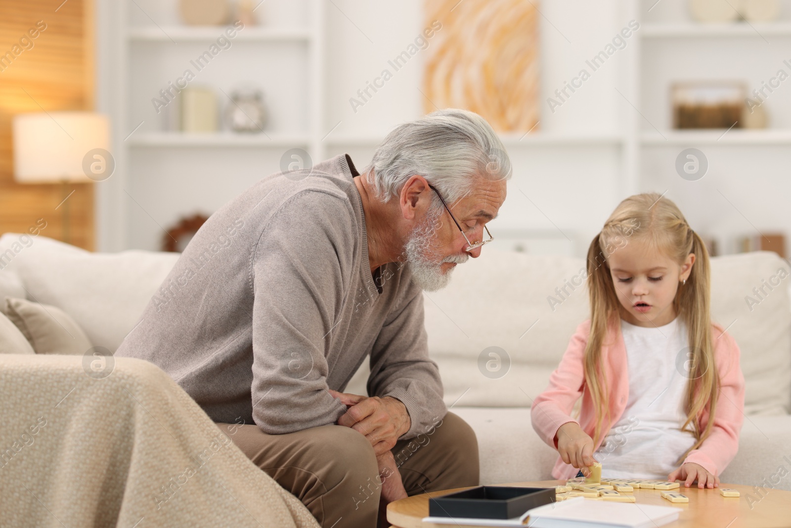 Photo of Grandpa and his granddaughter playing dominoes at table indoors