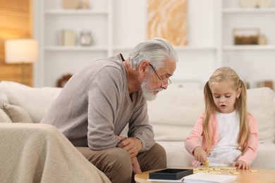 Grandpa and his granddaughter playing dominoes at table indoors