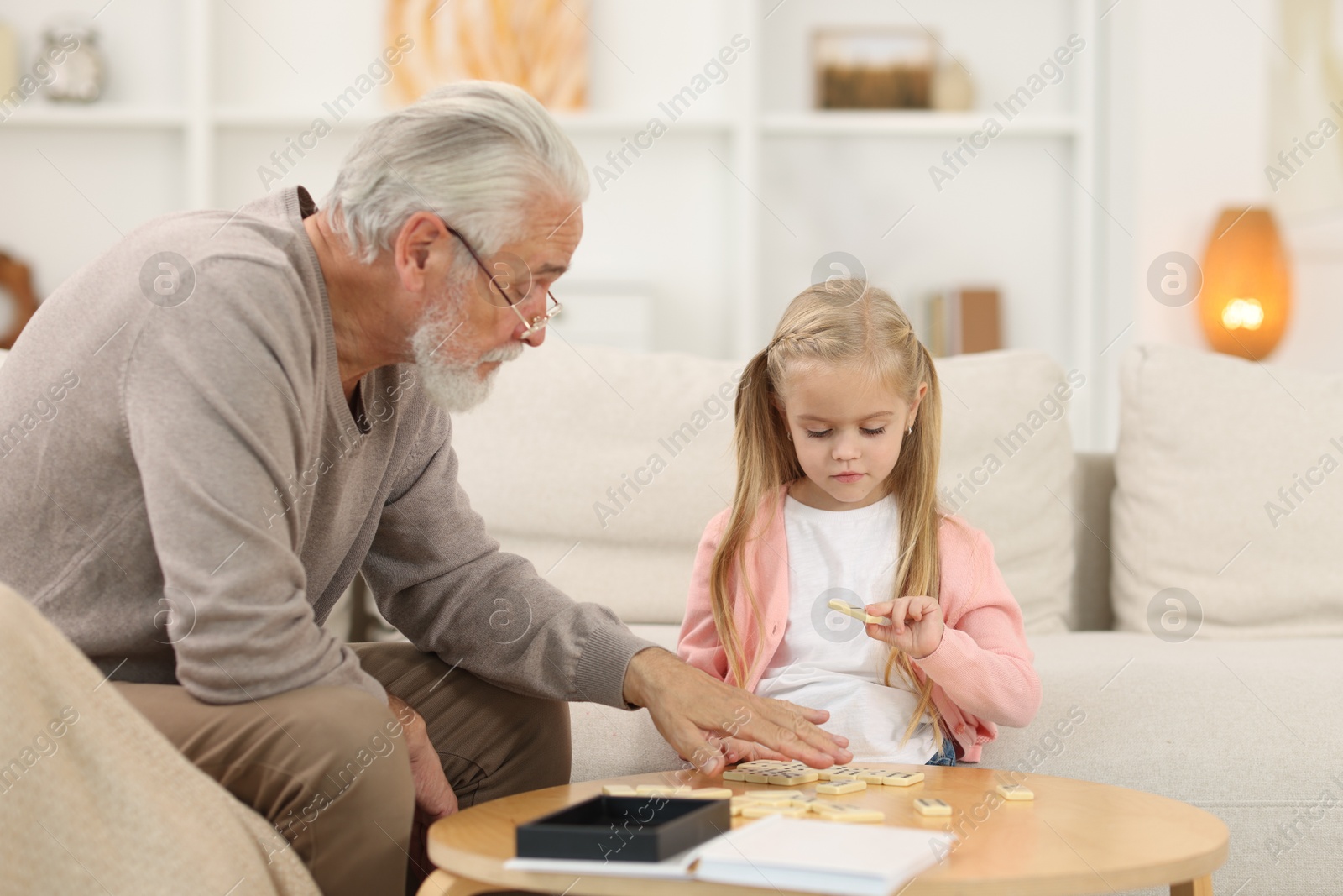 Photo of Grandpa and his granddaughter playing dominoes at table indoors