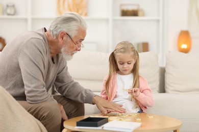 Photo of Grandpa and his granddaughter playing dominoes at table indoors